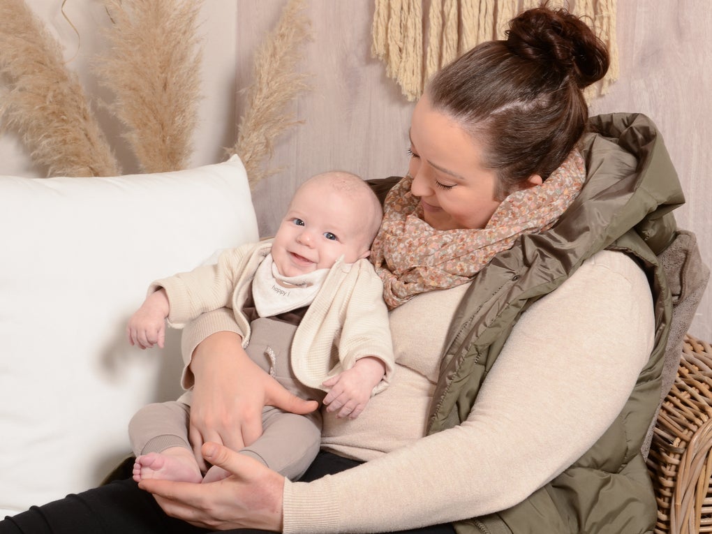 Eine Frau sitzt auf einem Rattanstuhl und hält ein Baby im Arm. Sie schaut das Kind liebevoll an, während das Baby in die Kamera lächelt. Beide tragen helle, aufeinander abgestimmte Kleidung in Beige- und Brauntönen. Im Hintergrund sind eine weiße Kissenlehne, Pampasgras und eine Makramee-Wanddekoration zu sehen.
Eine Frau sitzt auf einem Rattanstuhl und hält ein Baby im Arm. Sie schaut das Kind liebevoll an, während das Baby in die Kamera lächelt. Beide tragen helle, aufeinander abgestimmte Kleidung in Beige- und Brauntönen. Im Hintergrund sind eine weiße Kissenlehne, Pampasgras und eine Makramee-Wanddekoration zu sehen.