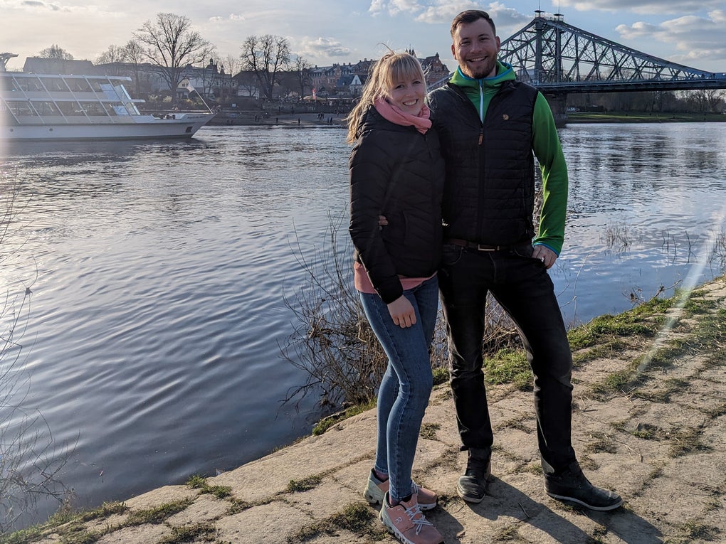 Eine Frau und ein Mann stehen an einem Flußufer, im Hintergrund sind ein Ausflugsschiff und eine Brücke zu sehen. Eine Frau und ein Mann stehen an einem Flußufer, im Hintergrund sind ein Ausflugsschiff und eine Brücke zu sehen.