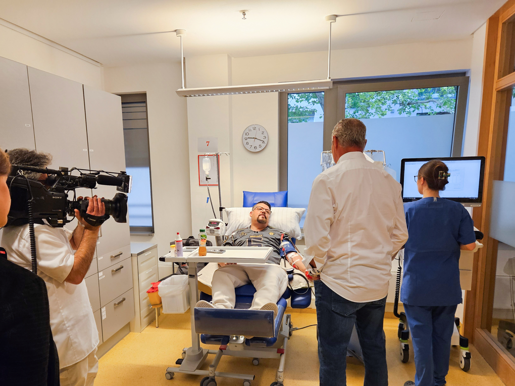 Ein Mann liegt in einem Krankenhausbett mit einem Mann auf einem Stuhl. Ein Mann liegt in einem Krankenhausbett mit einem Mann auf einem Stuhl.