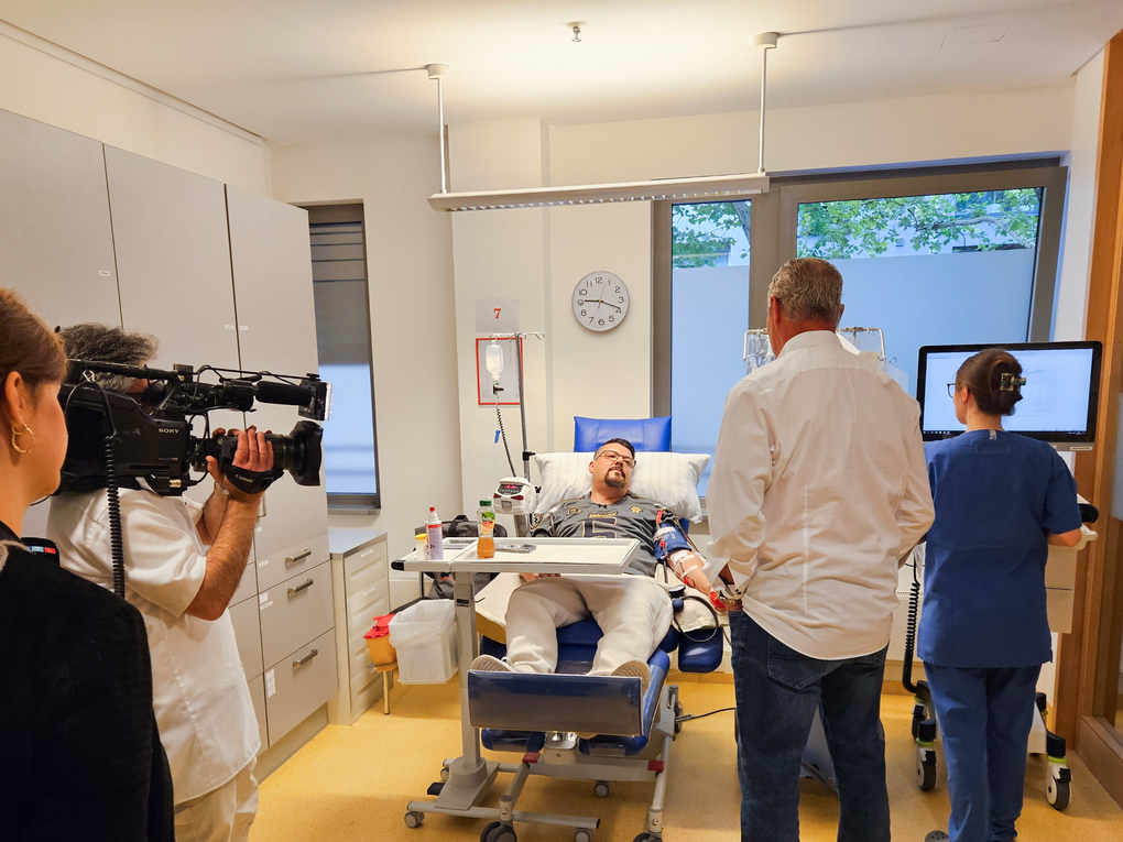 Ein Mann liegt in einem Krankenhausbett mit einem Mann auf einem Stuhl. Ein Mann liegt in einem Krankenhausbett mit einem Mann auf einem Stuhl.