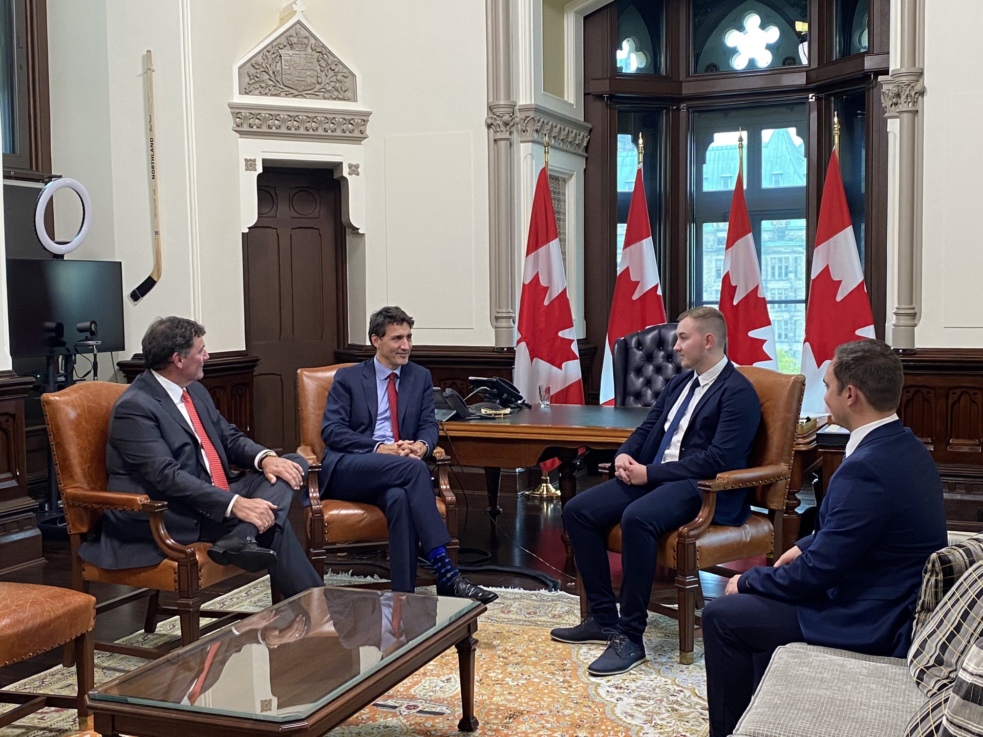 Eine Gruppe von Männern in Anzügen sitzt in einem Raum mit Kanada Fahnen Eine Gruppe von Männern in Anzügen sitzt in einem Raum mit Kanada Fahnen