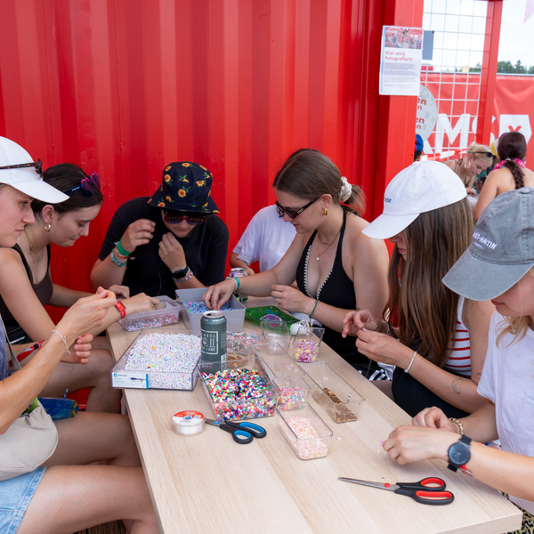 Eine Gruppe junger Leute bastelt am Stand der DKMS auf dem Southside Festival Armbänder Eine Gruppe junger Leute bastelt am Stand der DKMS auf dem Southside Festival Armbänder