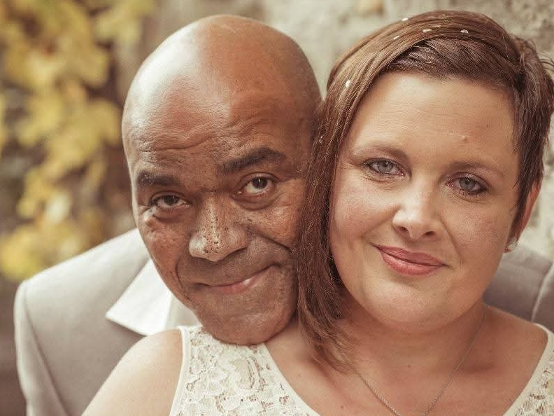 Ein verheiratetes Paar posiert für ein Hochzeitsfoto. Die Frau steht im Vordergrund, der Mann steht dahinter und umarmt die Frau Ein verheiratetes Paar posiert für ein Hochzeitsfoto. Die Frau steht im Vordergrund, der Mann steht dahinter und umarmt die Frau