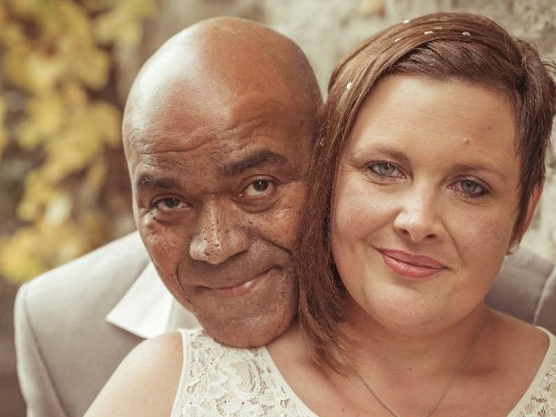 Ein verheiratetes Paar posiert für ein Hochzeitsfoto. Die Frau steht im Vordergrund, der Mann steht dahinter und umarmt die Frau Ein verheiratetes Paar posiert für ein Hochzeitsfoto. Die Frau steht im Vordergrund, der Mann steht dahinter und umarmt die Frau