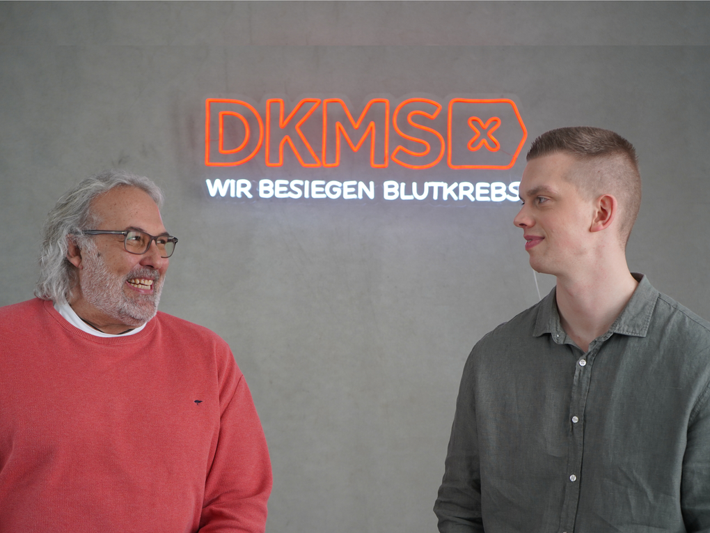 Zwei Männer stehen vor einem Leucht-Schild der DKMS Zwei Männer stehen vor einem Leucht-Schild der DKMS