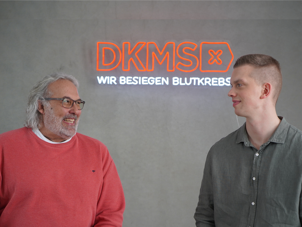 Zwei Männer stehen vor einem Leucht-Schild der DKMS Zwei Männer stehen vor einem Leucht-Schild der DKMS