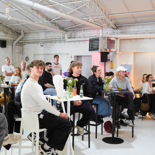 Eine Gruppe von Menschen sitzt an Tischen in einem Raum mit einer großen weißen Wand Eine Gruppe von Menschen sitzt an Tischen in einem Raum mit einer großen weißen Wand