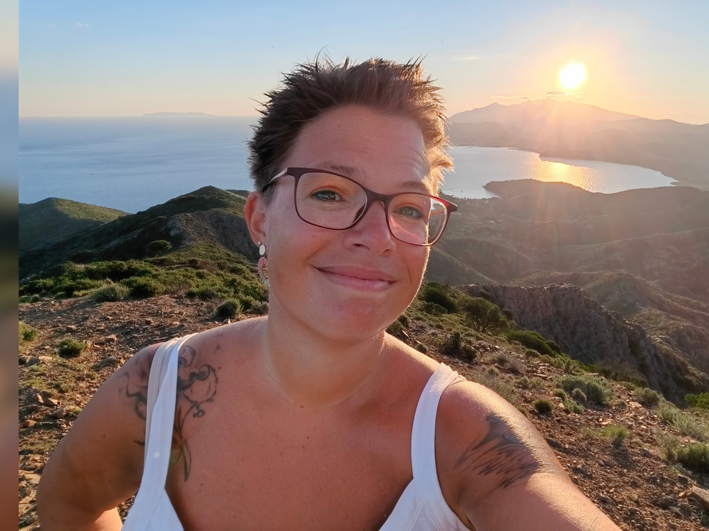 Eine Frau steht in sommerlicher Bekleidung auf einem Berg. Hinter ihr geht die Sonne unter. Eine Frau steht in sommerlicher Bekleidung auf einem Berg. Hinter ihr geht die Sonne unter.