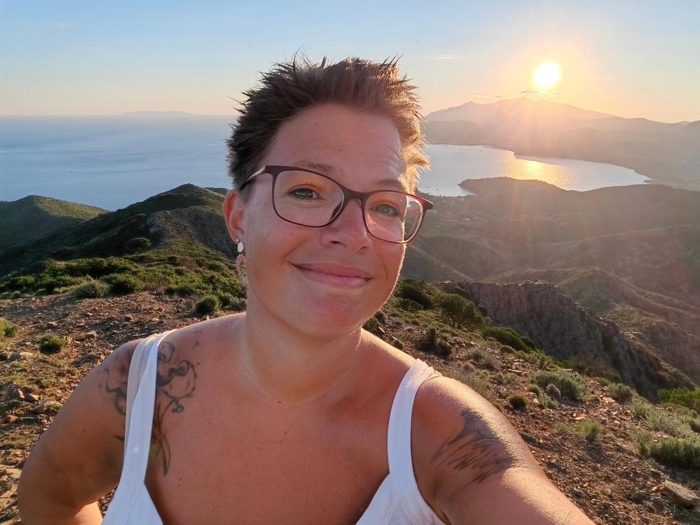 Eine Frau steht in sommerlicher Bekleidung auf einem Berg. Hinter ihr geht die Sonne unter. Eine Frau steht in sommerlicher Bekleidung auf einem Berg. Hinter ihr geht die Sonne unter.