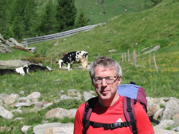 Ein Mann steht vor einem Fluss mit einer Kuh im Hintergrund Ein Mann steht vor einem Fluss mit einer Kuh im Hintergrund