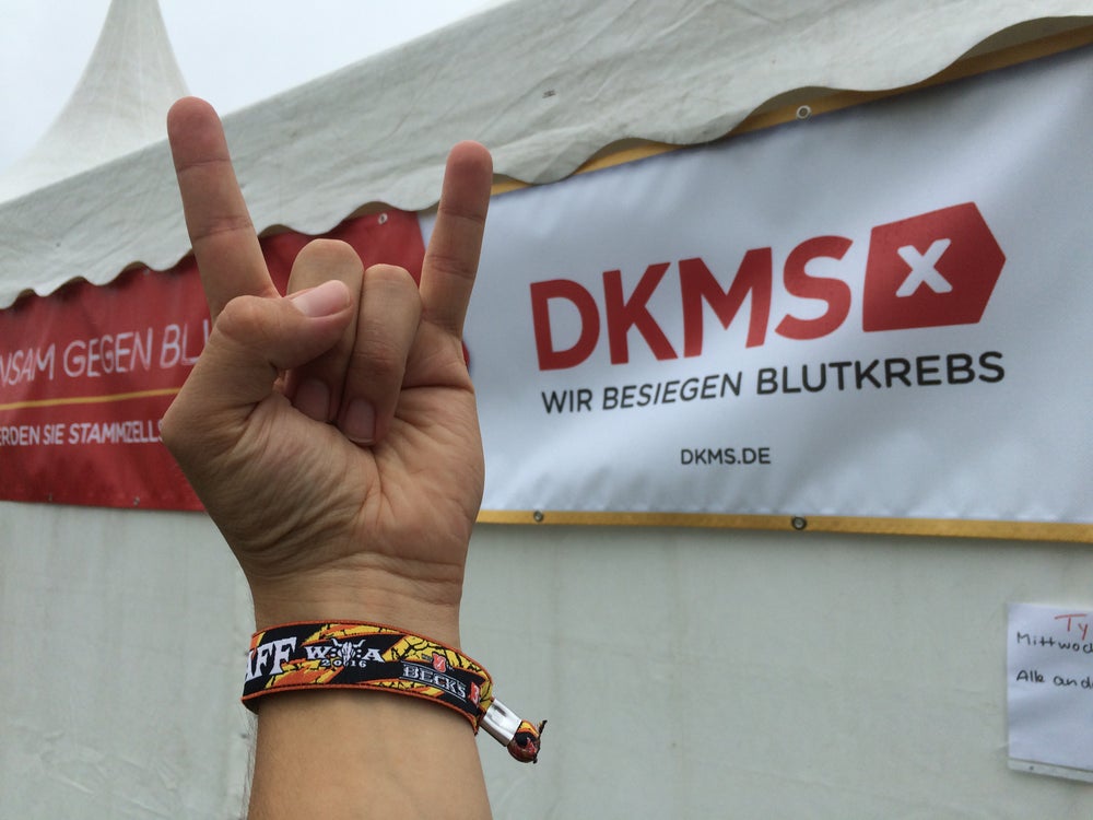 heavy-metal Handzeichen vor einem DKMS Banner heavy-metal Handzeichen vor einem DKMS Banner