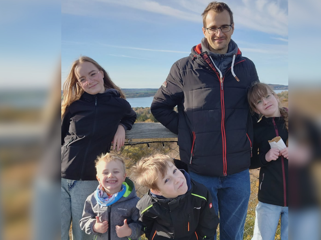 Ein Mann lehnt an einem hölzernen Geländer. Zwei junge Mädchen und zwei Jungen stehen bei ihm. Ein Mann lehnt an einem hölzernen Geländer. Zwei junge Mädchen und zwei Jungen stehen bei ihm.