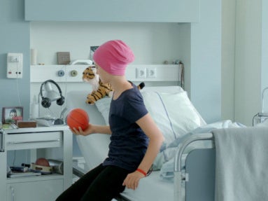 Screenshot aus einem Werbespot. Rinah sitzt auf einem Bett eines Krankenhauszimmers. Links unten im Bild der Text vox.de/dkms Screenshot aus einem Werbespot. Rinah sitzt auf einem Bett eines Krankenhauszimmers. Links unten im Bild der Text vox.de/dkms