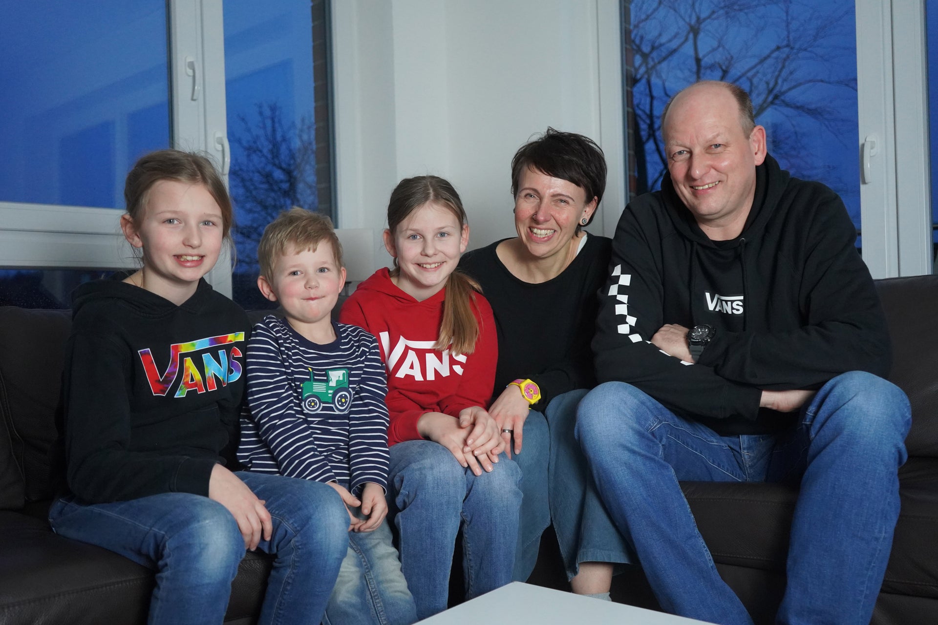 eine Familie sitzt auf einer Couch und posiert für ein Foto, alle lächeln eine Familie sitzt auf einer Couch und posiert für ein Foto, alle lächeln