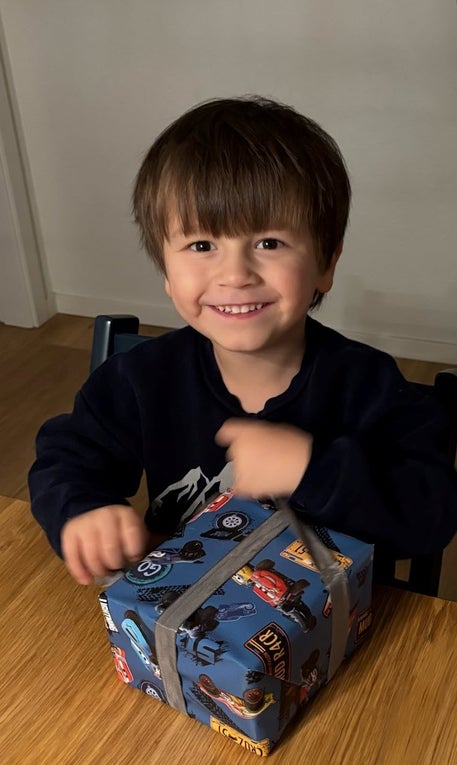 Ein kleiner junge mit dunkeln Haaren sitzt an einem Tisch und packt ein Geschenk aus. Ein kleiner junge mit dunkeln Haaren sitzt an einem Tisch und packt ein Geschenk aus.