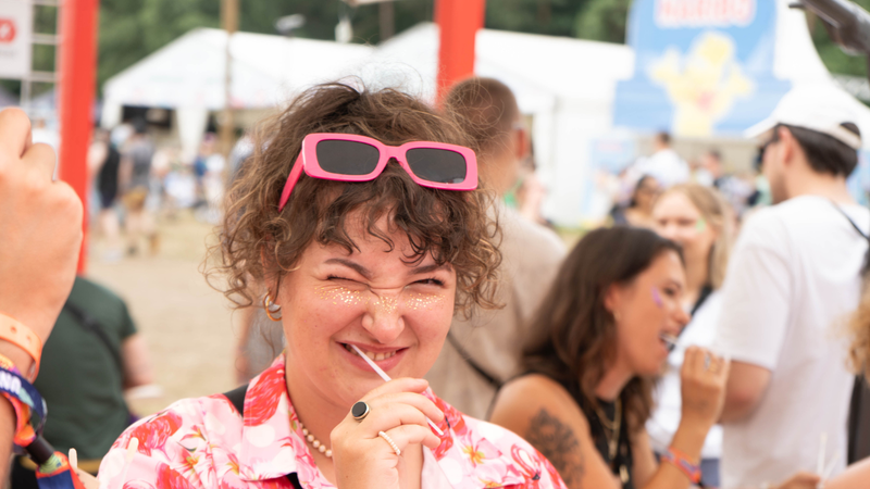 Eine junge Frau steht auf einem Festivalgelände und macht einen Wangenabstrich Eine junge Frau steht auf einem Festivalgelände und macht einen Wangenabstrich