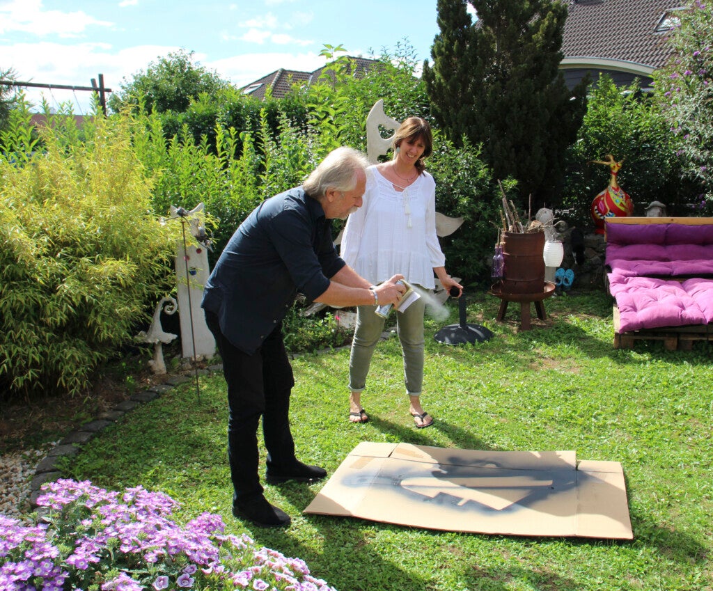 Henning Krautmacher und Ela sprühen ein Bild auf Karton in einem Garten Henning Krautmacher und Ela sprühen ein Bild auf Karton in einem Garten