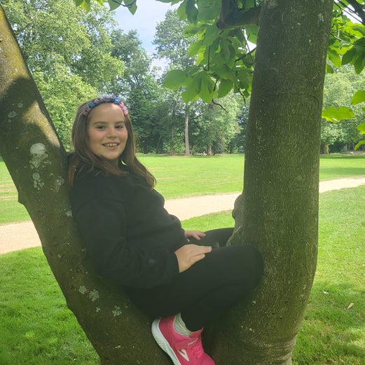 Man sieht Patientin Melina, die in einem Park auf einem Baum sitzt.