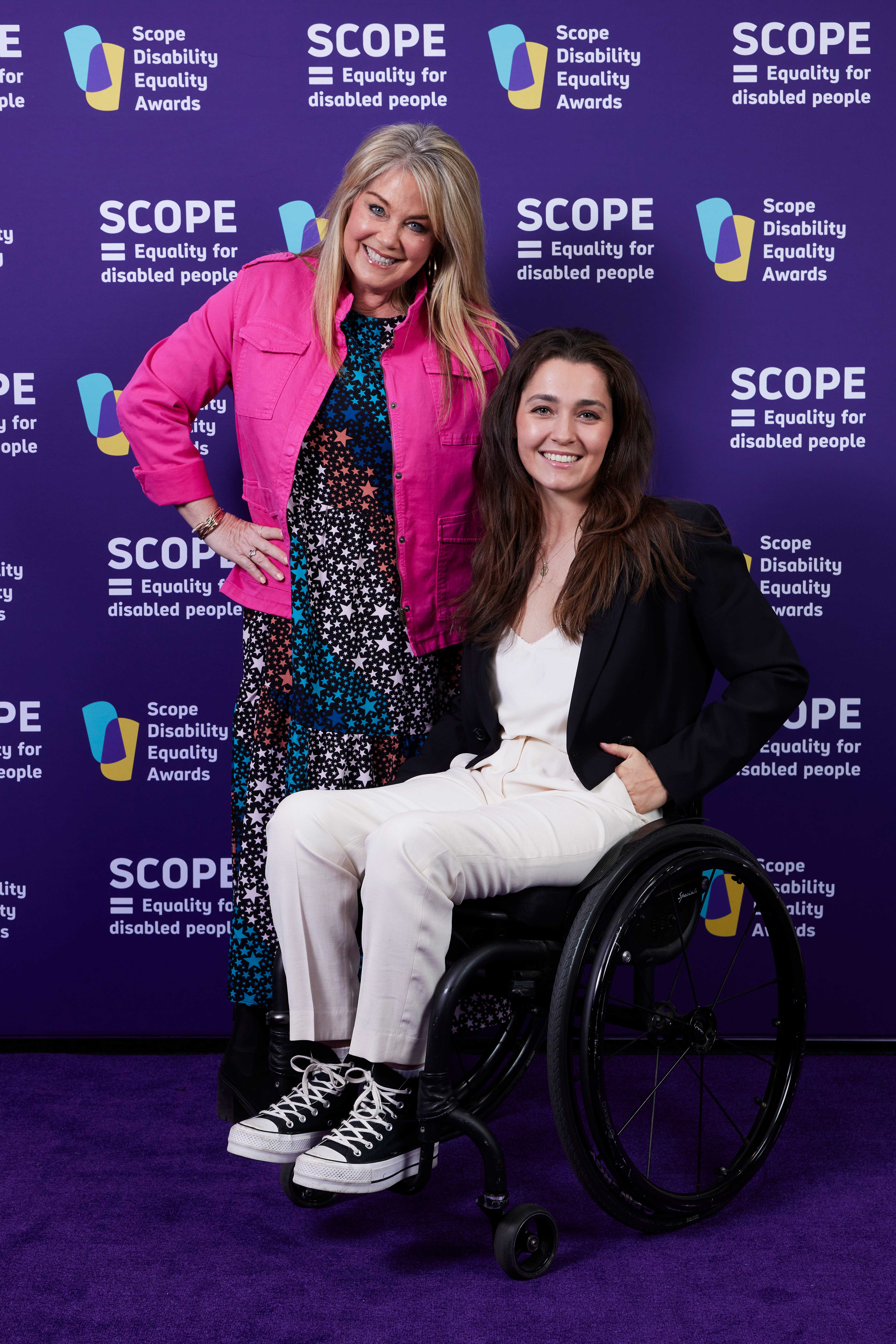 A woman in a wheelchair posing with another woman in a purple background