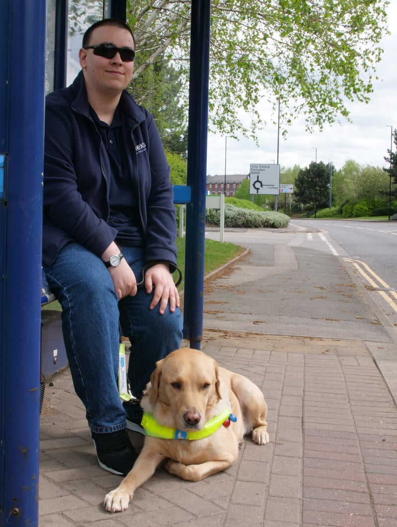 A young man with his guide dog at a bus stop