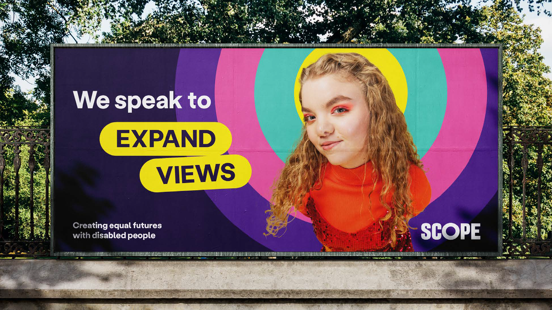 Billboard with photo overlaid multi-coloured amplification circle. To the left, text says 'we speak to' then in 2 lozenges 'expand views'. Our logo in bottom right and tagline bottom left.