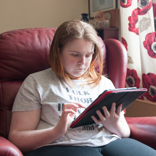 A young woman sitting at home in a seat using an iPad