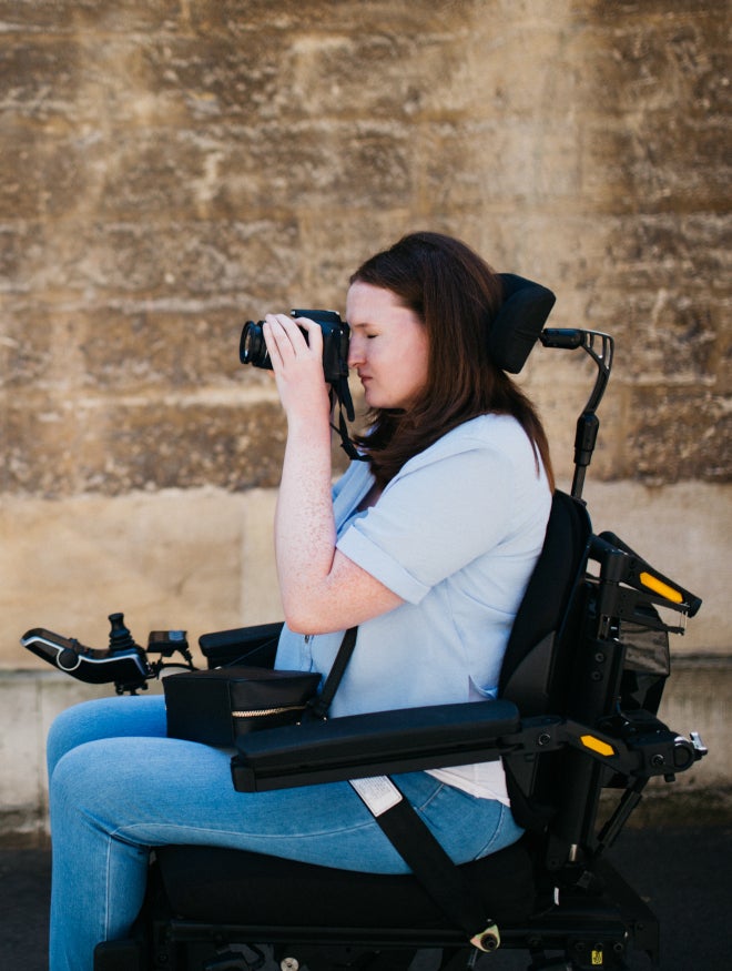 A young woman in a power chair taking a photograph on the street