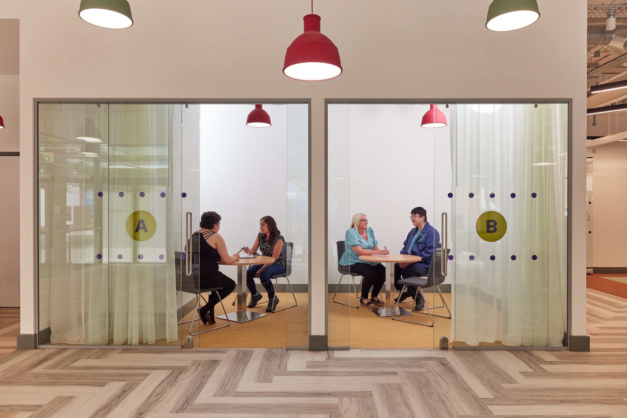 Meeting room A and B, with advisers and customers meeting inside them. Glass doors and curtains ensure privacy.