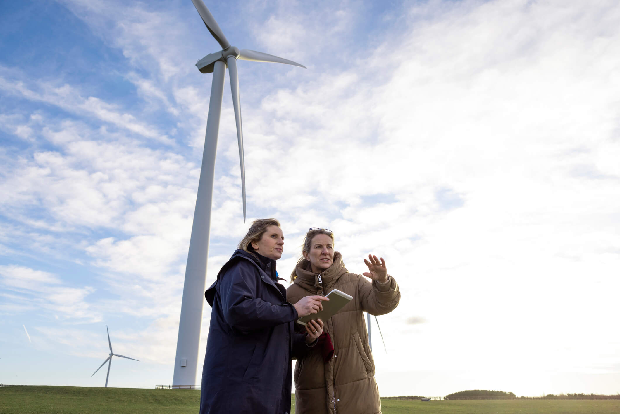 two females standing in front of a large wind turbine