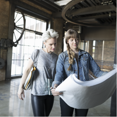 Two women looking at blueprints in warehouse office for business relocation