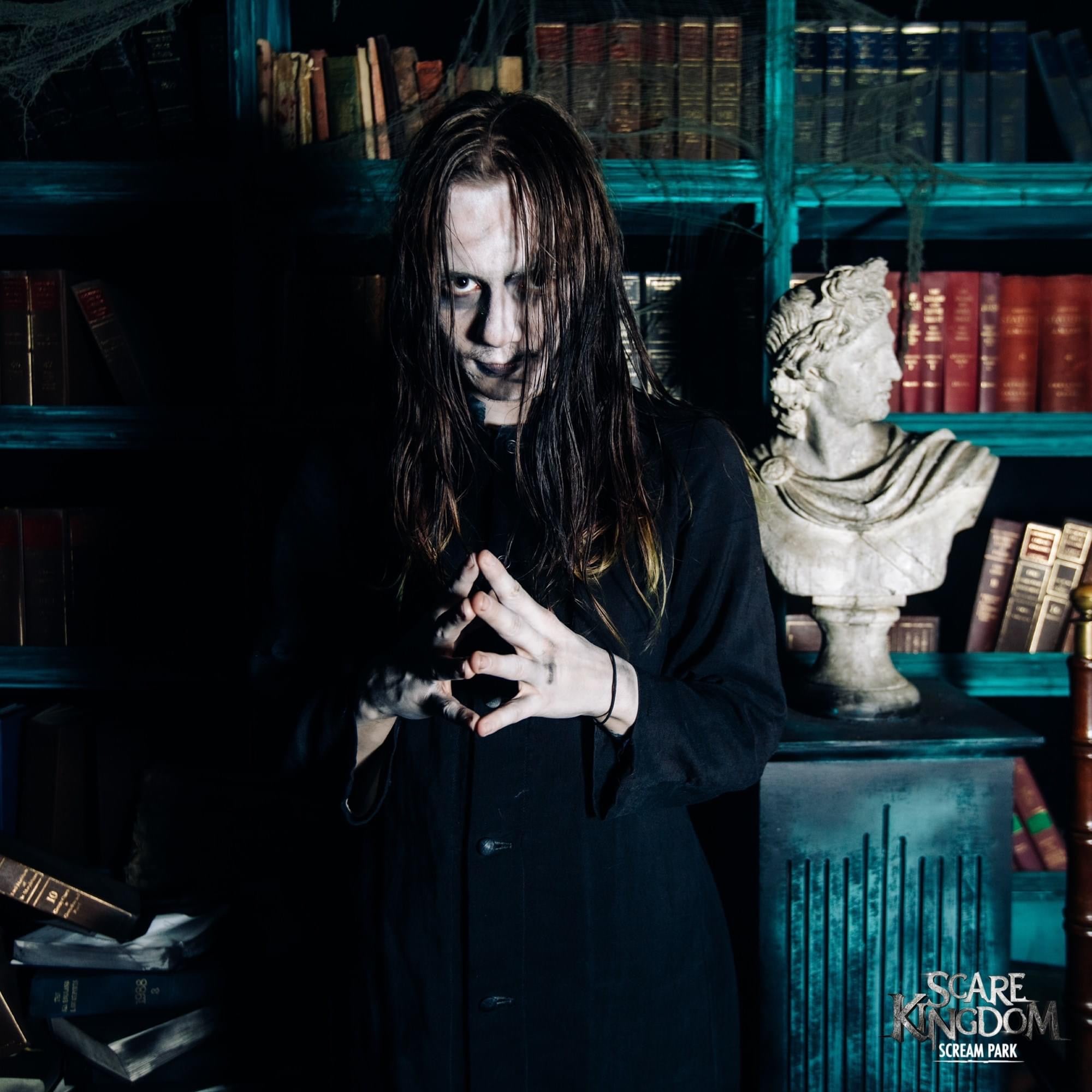 A scare maze actor posing as a vampire beside a bookcase 