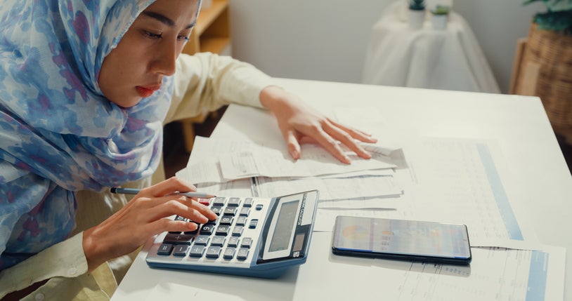 A business owner has papers and a calculator on her desk while working out if she can afford her business energy bills