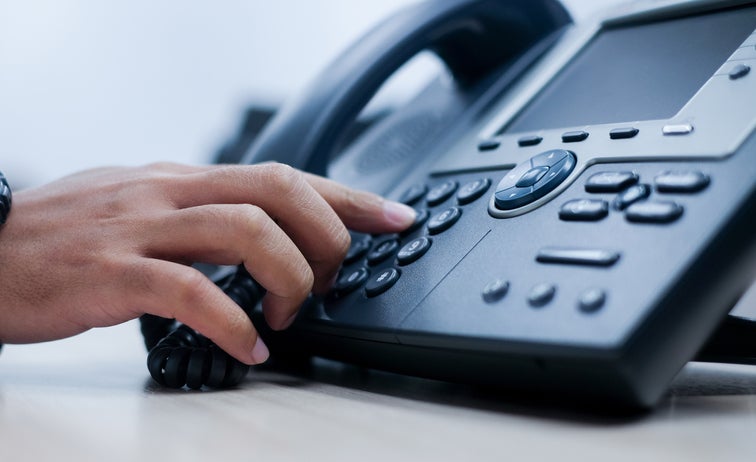  The hand of an employee presses a button on a business landline telephone