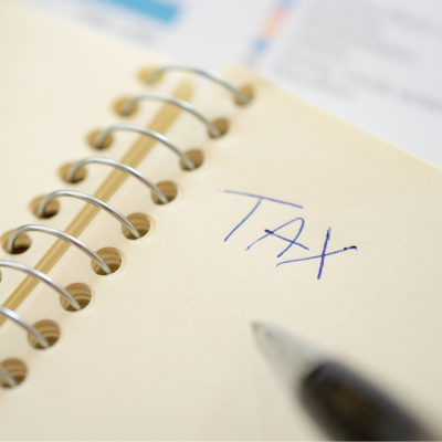 White notepad with blue pen and handwritten message saying "TAX" in upper case letters