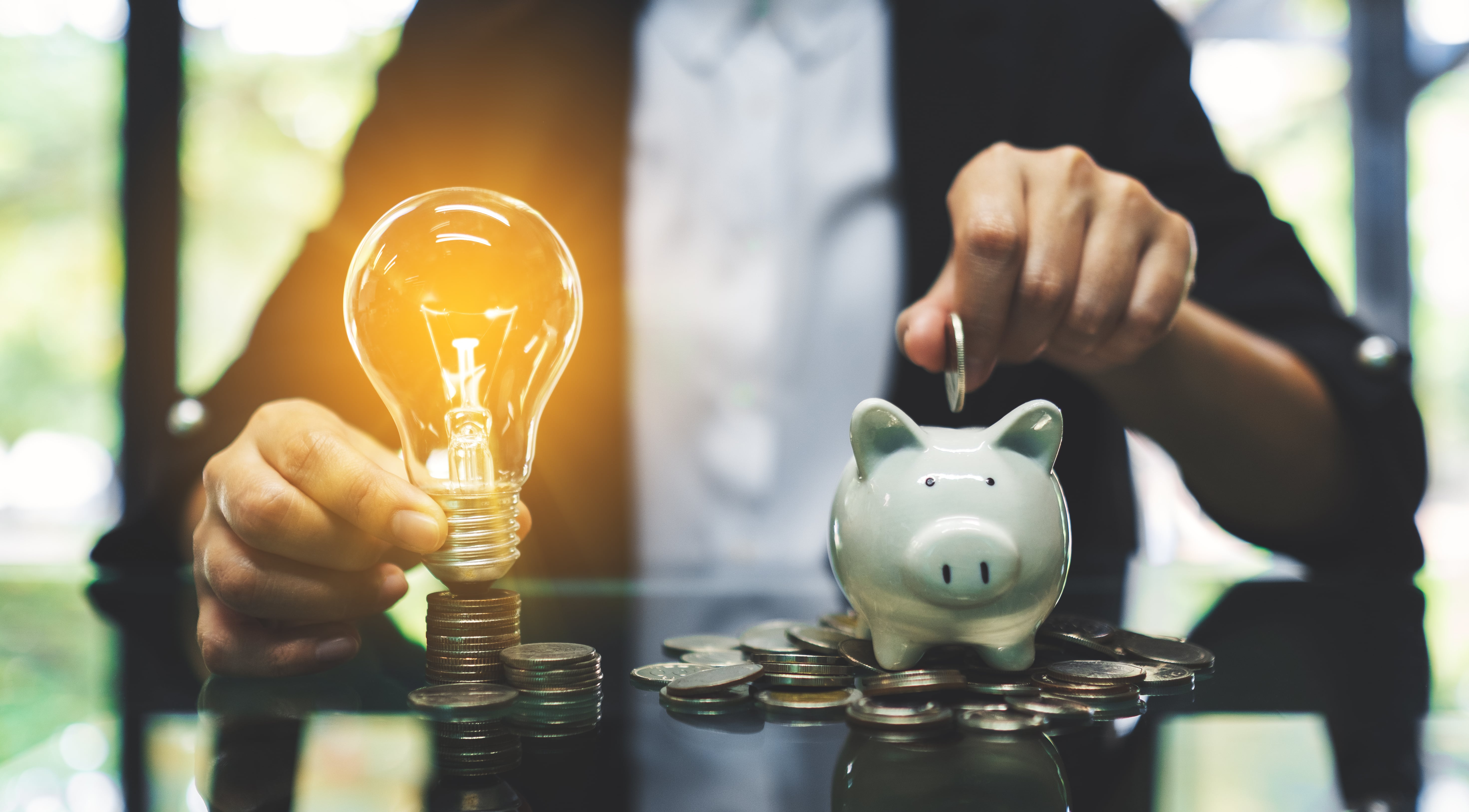 table with person holding lightbulb and putting coins into a piggybank