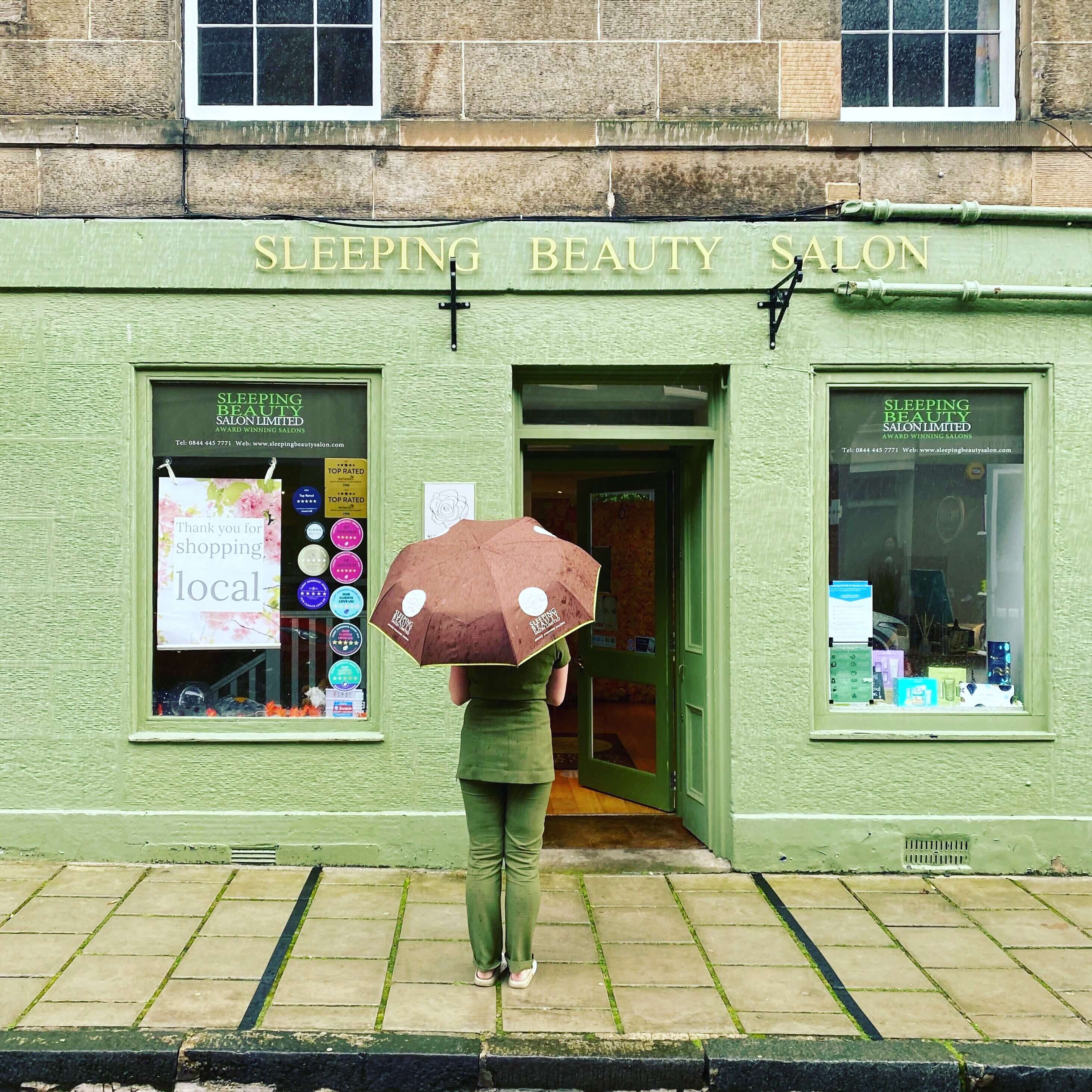 A customer with a pink umbrella stands outside Sleeping Beauty Salon