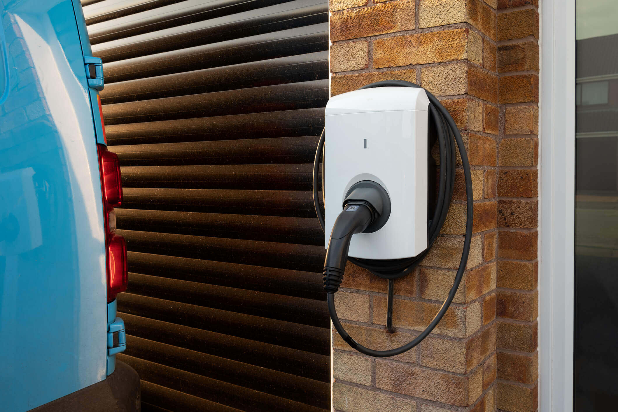 electric charging point attached to a house with a garage and blue parked car