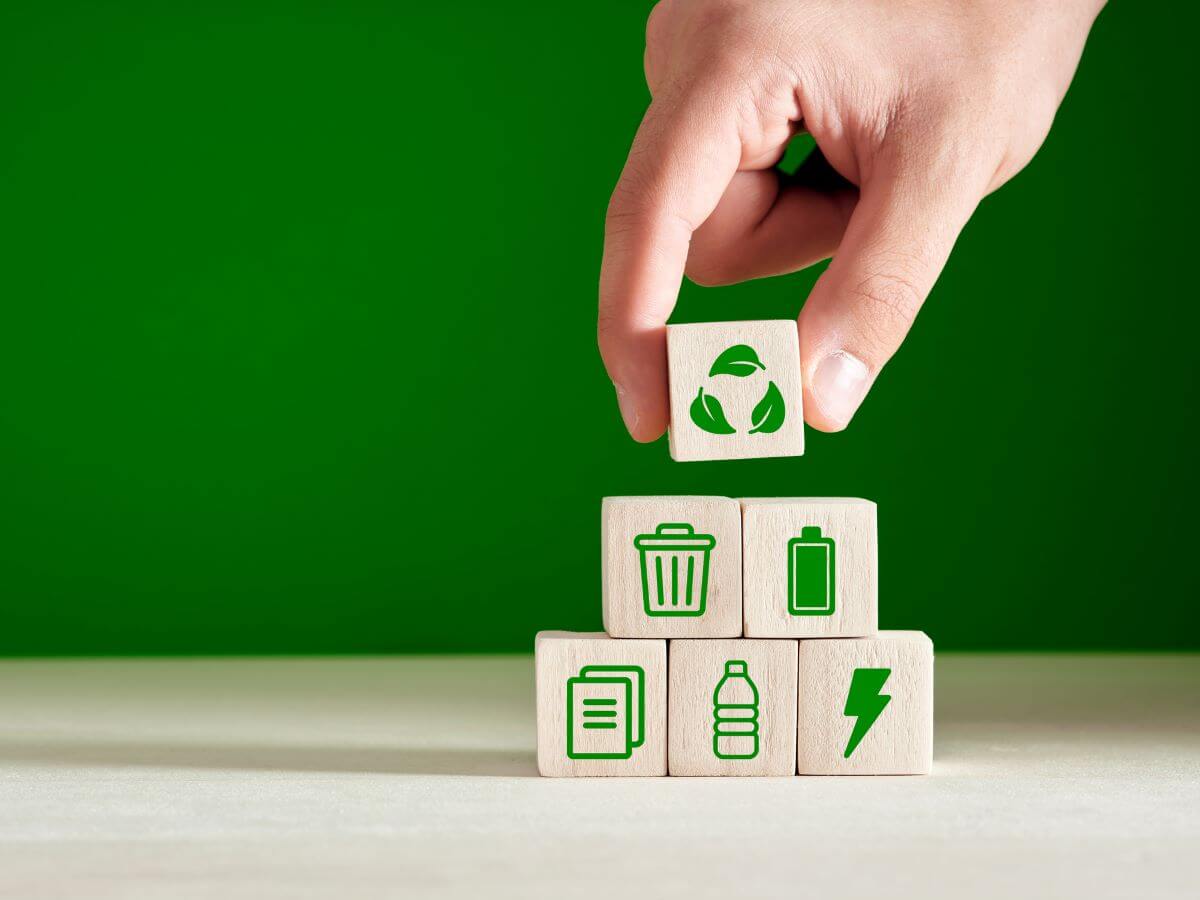 A business owner's hand places blocks that have recycling icons on, such as a battery, a bottle, and a bin.