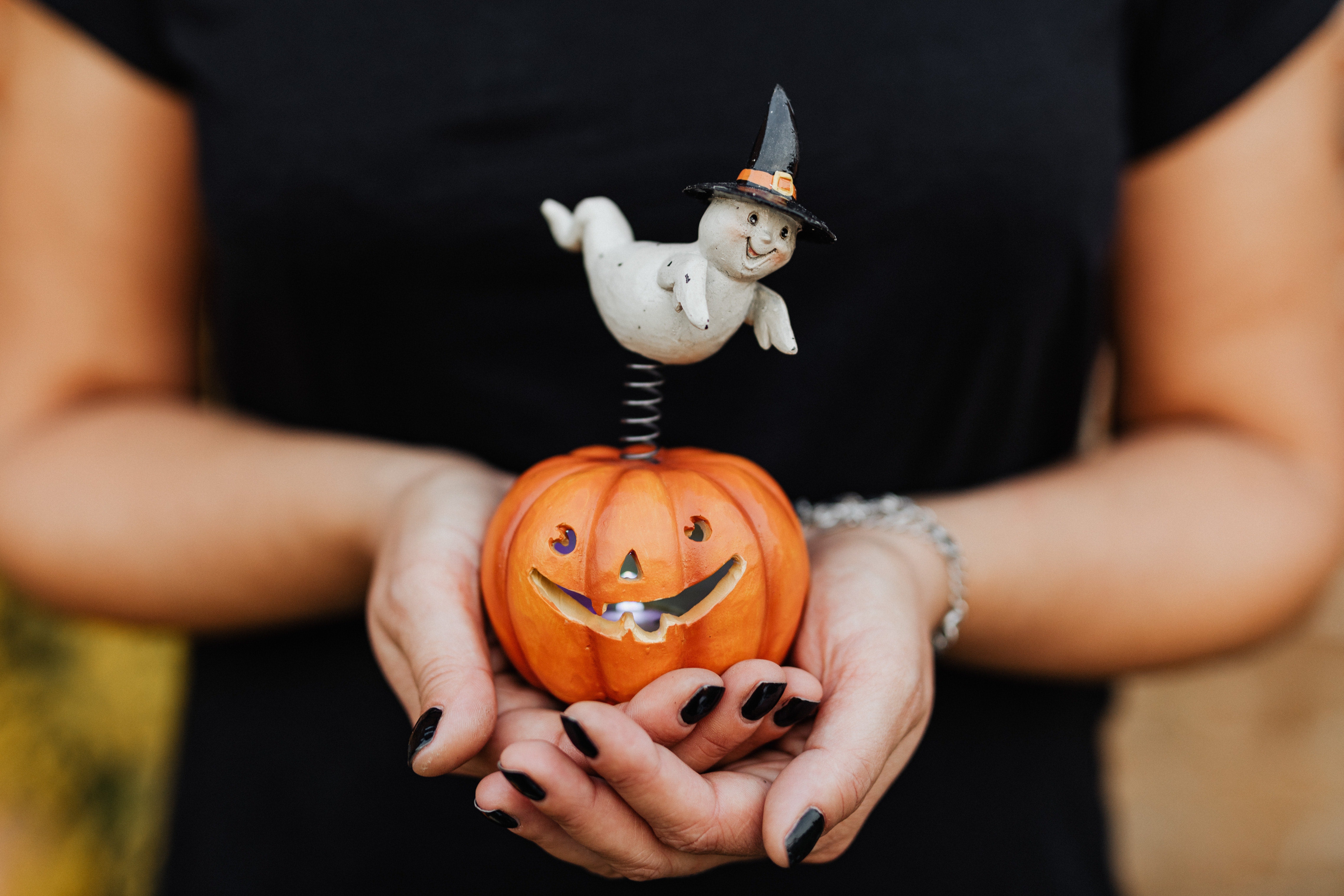 Person holding a mini carved pumpkin with a ghost on top 