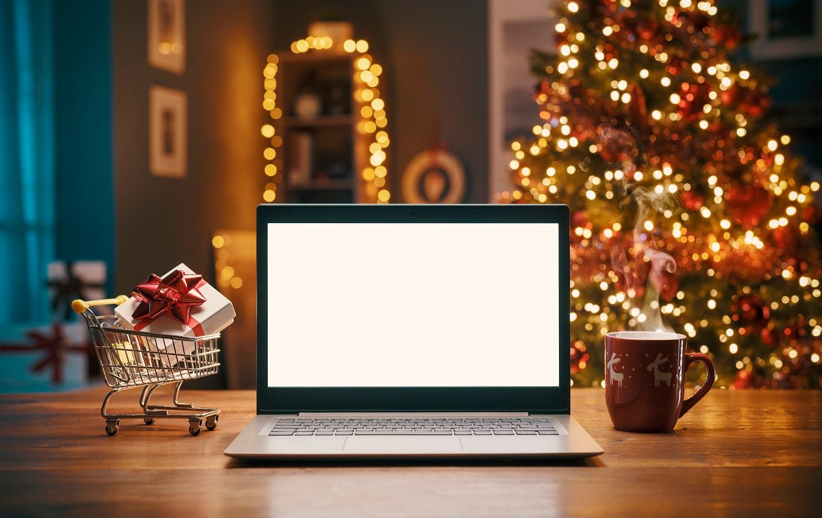 An open laptop in front of a Christmas tree decorated with twinkling lights