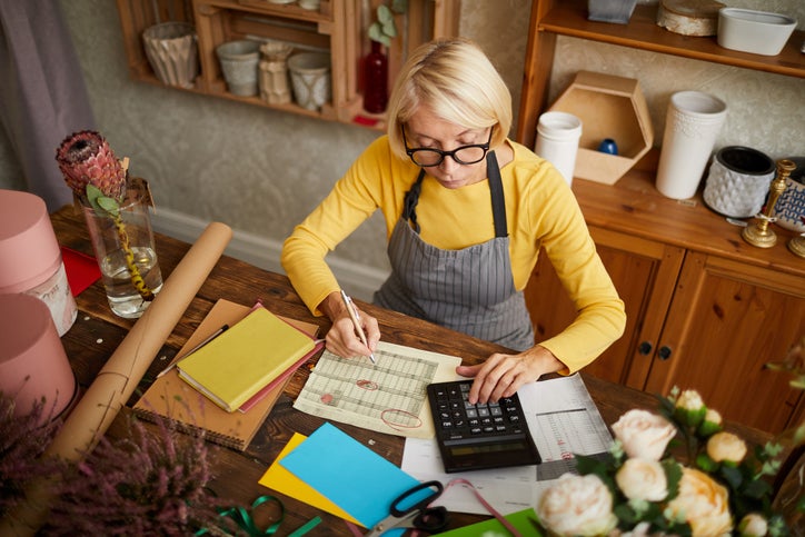 A small business owner sits in her shop with a calendar, papers, and calculator as she prepares for the end of the financial year.