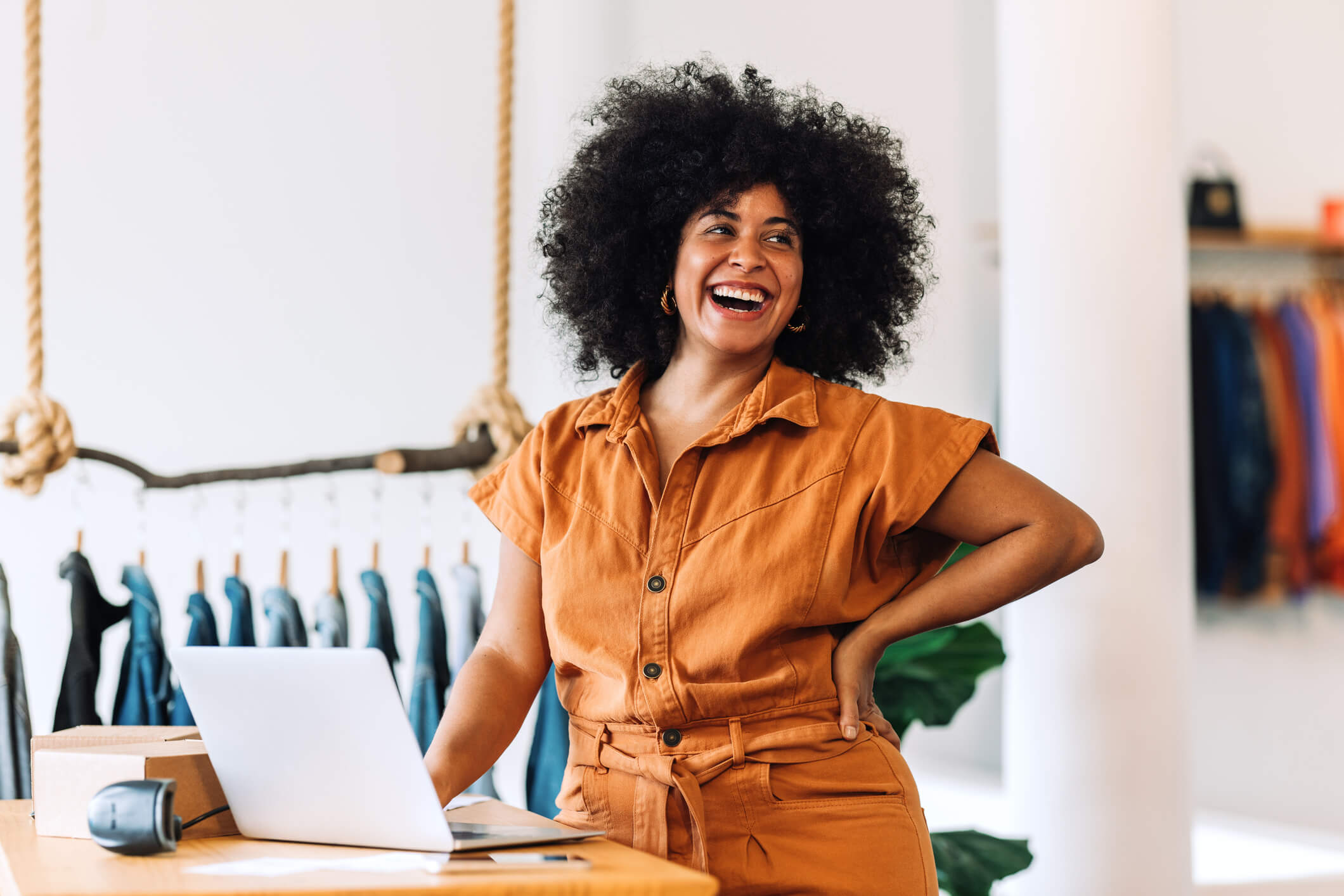 Woman with laptop behind counter in a clothes shop smiling