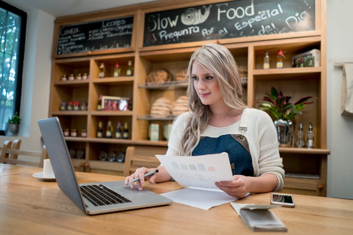 A small business owner sits at her counter with a laptop and papers working out the best way to fund growth