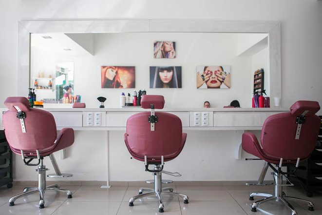 Hair salon with big mirror on the wall and three pink salon chairs facing the mirror