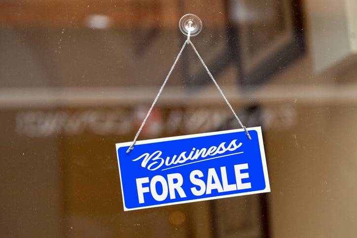 A blue 'business for sale' sign hanging on a window