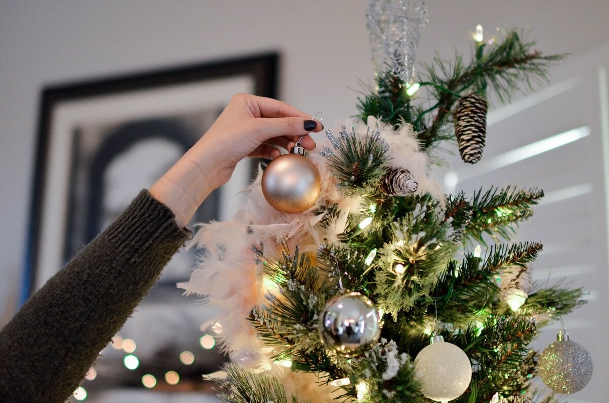 A person wearing a black long sleeved jumper decorates a Christmas tree