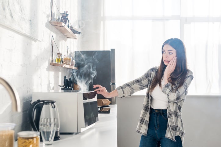 woman looking at smoke coming out of her broken microwave in her kitchen