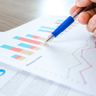 Hand holds blue pen pointing at bar chart on paper sheet showing business finance fees