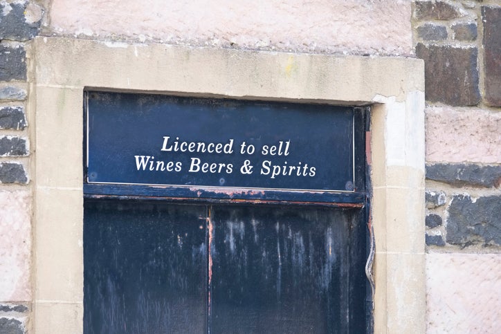 a black door to a pub in a stone wall. A sign above the door shows it has a licence to sell alcohol in the uk