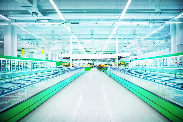 An empty isle in a supermarket showing green food cabinets that are brightly lit.